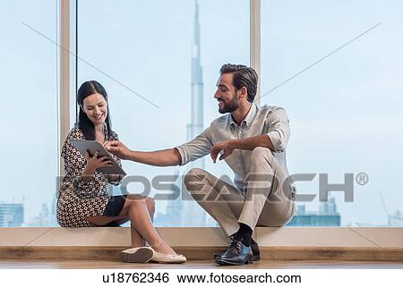 Stock Photograph - Businesswoman and man sitting at window, Dubai, United Arab Emirates. Fotosearch