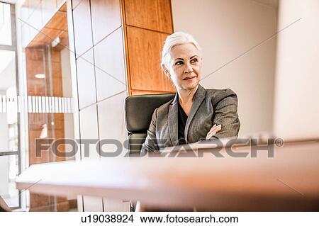 Businesswoman sitting at desk arms crossed looking away View Large Photo Image Picture - Businesswoman sitting at desk arms crossed looking away. Fotosearch