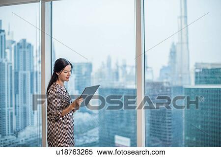 Stock Photography - Businesswoman using digital tablet at window, Dubai, United Arab Emirates. Fotosearch