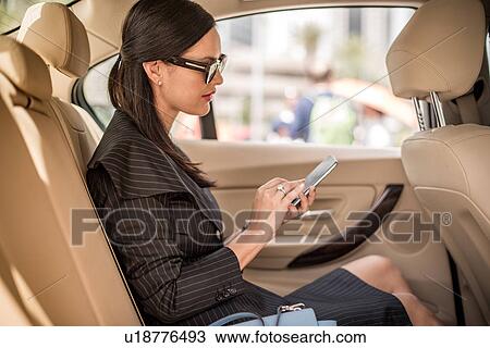 Stock Image - Businesswoman using smartphone touchscreen in car backseat, Dubai, United Arab Emirates. Fotosearch