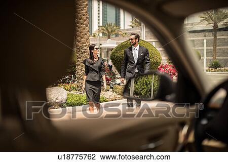 Stock Image - Car window view of businesswoman and man walking outside hotel, Dubai, United Arab Emirates. Fotosearch