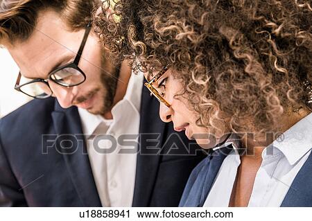 Stock Image - Close up of businesswoman and businessman reading paperwork outside office. Fotosearch