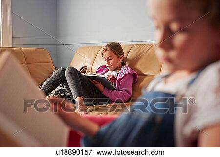 Stock Photo - Close up of girl and her sister reading books in living room. Fotosearch