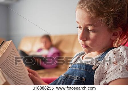 Stock Photography - Close up of girl and her sister reading books in living room. Fotosearch