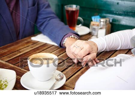 Stock Photo - Close up of mature dating couple holding hands at sidewalk cafe table. Fotosearch