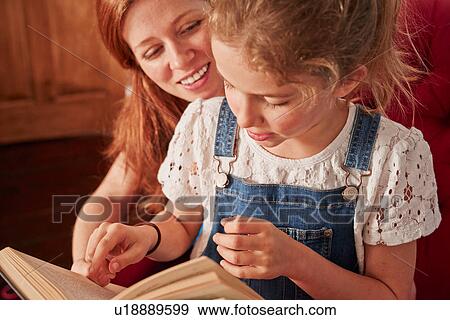 Stock Photo - Close up of mid adult woman reading book with daughter on armchair. Fotosearch