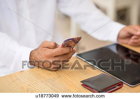 Stock Photo - Close up of middle eastern man's hands using smartphone at cafe, Dubai, United Arab Emirates. Fotosearch
