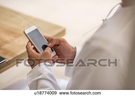 Stock Photo - Close up of middle eastern man's hands using smartphone touchscreen at cafe, Dubai, United Arab Emirates. Fotosearch
