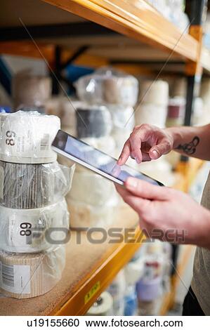 Stock Image - Close up of worker stock taking using digital tablet touchscreen in roller blind factory. Fotosearch