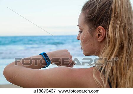 Stock Photo - Close up of young female runner checking smartwatch time on beach, Dominican Republic, The Caribbean. Fotosearch