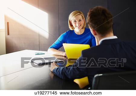 Stock Photography - Colleagues sitting at desk having meeting smiling. Fotosearch