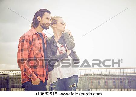 Stock Photography - Cool mid adult couple looking out from rooftop parking lot. Fotosearch