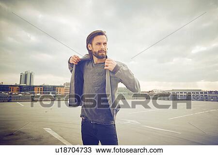Cool mid adult man putting on jacket at rooftop parking lot View Large Photo Image Stock Image - Cool mid adult man putting on jacket at rooftop parking lot. Fotosearch