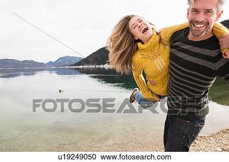 Stock Image - Couple fooling around beside lake, smiling, German Alps, Germany. Fotosearch