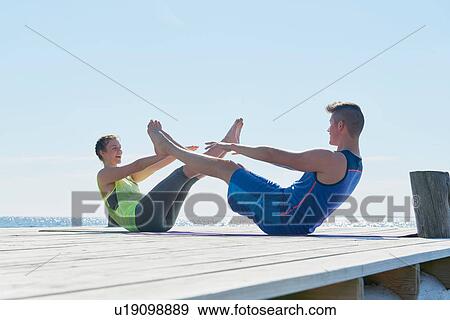 Stock Photo - Couple on pier face to face, legs raised doing sit ups. Fotosearch