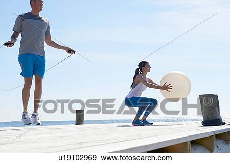 Stock Photo - Couple on pier using skipping rope and exercise ball. Fotosearch