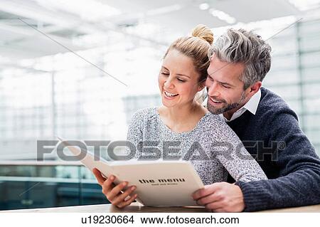 Picture - Couple sitting together at table, looking at menu. Fotosearch