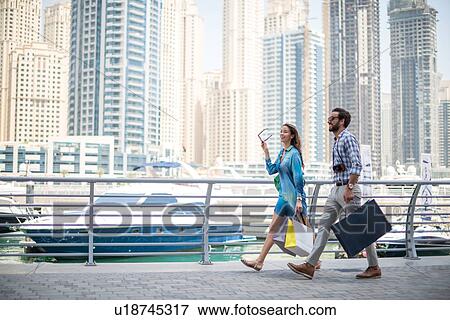Stock Photo - Couple strolling on waterfront carrying shopping bags, Dubai, United Arab Emirates. Fotosearch