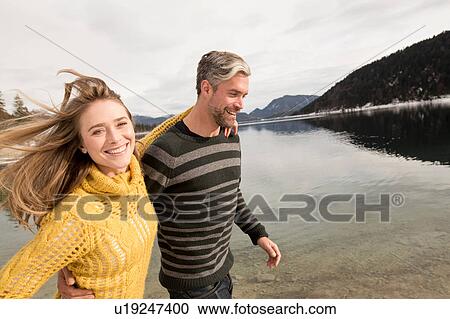 Stock Image - Couple walking beside lake, smiling, German Alps, Germany. Fotosearch