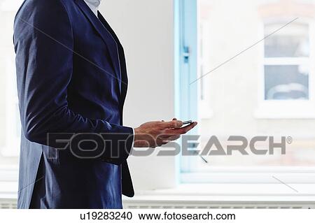 Stock Image - Cropped side view of man wearing suit holding smartphone. Fotosearch