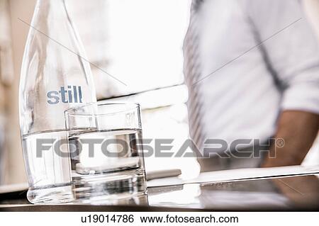 Stock Photograph - Cropped view of businessmans mid section with glass bottle of water and drinking glass. Fotosearch