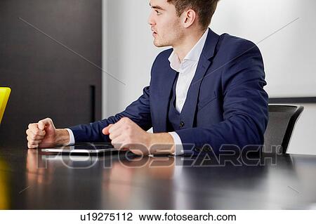 Stock Image - Cropped view of man sitting at desk with digital tablet looking away. Fotosearch