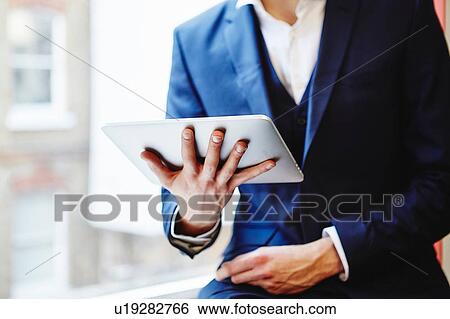 Stock Photograph - Cropped view of man wearing suit holding digital tablet. Fotosearch