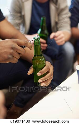 Stock Image - Cropped view of mans hands opening bottle of beer. Fotosearch