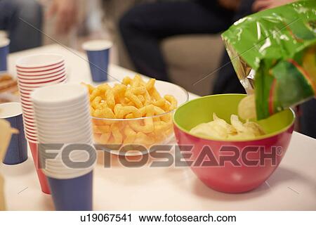 Stock Image - Cropped view of table with disposable cups and bowls of potato chips and snacks. Fotosearch