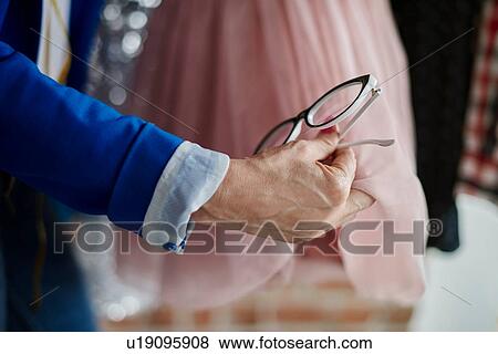 Cropped view of woman hand holding eyeglasses examining chiffon dress View Large Photo Image Stock Photo - Cropped view of woman hand holding eyeglasses examining chiffon dress. Fotosearch