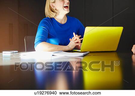 Stock Image - Cropped view of woman sitting at desk with laptop computer laughing. Fotosearch