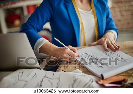 Cropped view of woman sitting at desk sketching fashion design View Large Photo Image Stock Photography - Cropped view of woman sitting at desk sketching fashion design. Fotosearch
