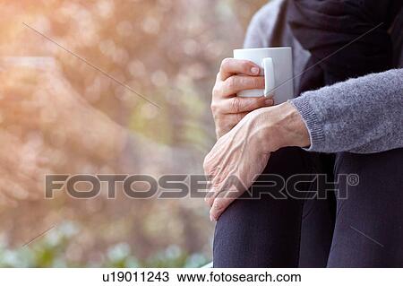 Cropped view of woman sitting by window holding coffee cup hugging knees View Large Photo Image Stock Image - Cropped view of woman sitting by window holding coffee cup hugging knees. Fotosearch