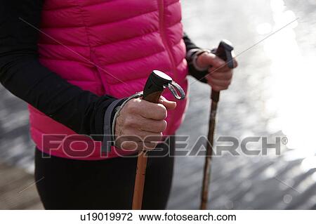 Stock Image - Cropped view of womans mid section holding nordic walking poles. Fotosearch