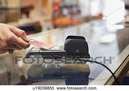 Stock Photography - Cropped view of womens hand using credit card to make contactless payment on chip and pin machine. Fotosearch