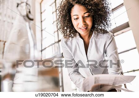 Picture - Curly haired business woman looking down at paperwork smiling. Fotosearch