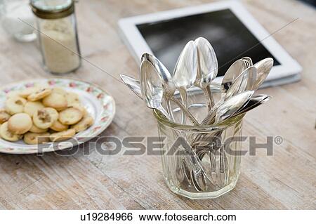 Stock Photograph - Digital tablet, plate of cookies and jar of spoons on wooden surface. Fotosearch