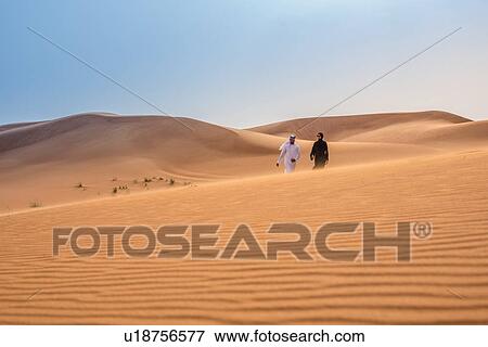 Distant view of couple wearing traditional middle eastern clothes walking on desert dune, Dubai, United Arab Emirates View Large Photo Image Stock Photo - Distant view of couple wearing traditional middle eastern clothes walking on desert dune, Dubai, United Arab Emirates. Fotosearch
