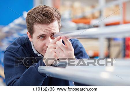 Stock Image - Factory worker inspecting metal rods in roller blind factory. Fotosearch