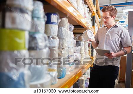 Stock Image - Factory worker stock taking using digital tablet in roller blind factory. Fotosearch