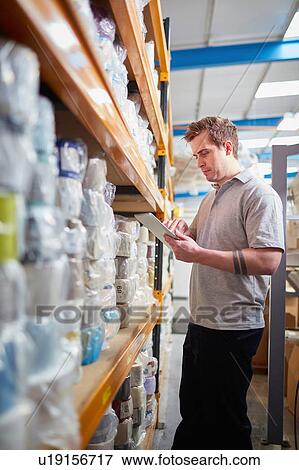 Stock Photo - Factory worker stock taking using digital tablet touchscreen in roller blind factory. Fotosearch