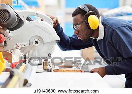 Stock Image - Factory worker using circular saw in roller blind factory. Fotosearch
