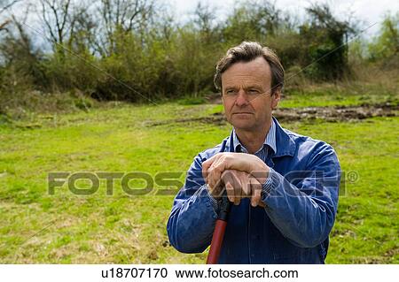 Stock Image - Farmer leaning on pitch fork in field. Fotosearch