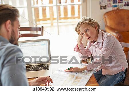Stock Image - Father helping son with homework in home office. Fotosearch