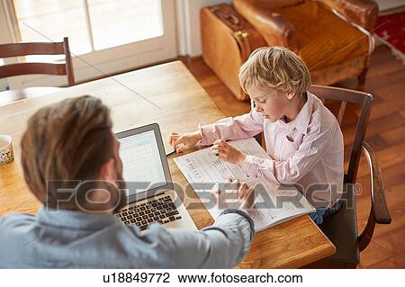 Stock Image - Father helping son with homework in home office. Fotosearch