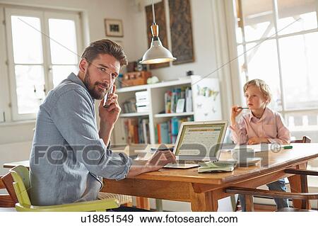 Stock Photo - Father on phone while working in home office with son. Fotosearch