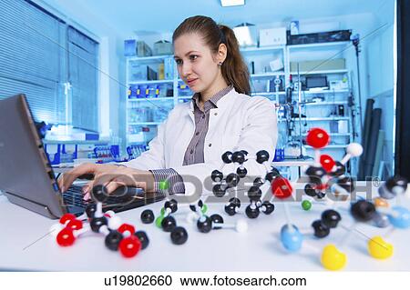 Stock Image - Female chemist using laptop in lab. Fotosearch