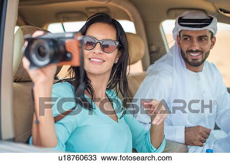 Stock Image - Female tourist in off road vehicle in desert taking photographs, Dubai, United Arab Emirates. Fotosearch