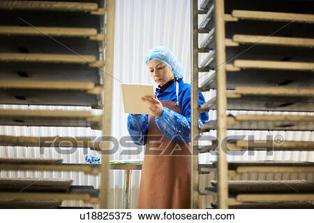 Stock Photography - Female worker using digital tablet in underground tunnel seed tray nursery, London, UK. Fotosearch