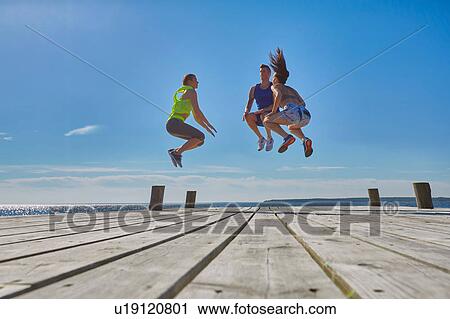 Friends on pier jumping in mid air View Large Photo Image Stock Image - Friends on pier jumping in mid air. Fotosearch